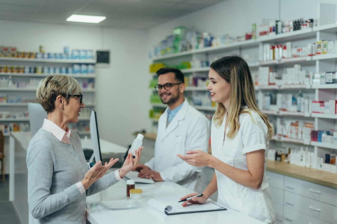pharmacist working on a computer while female pharmacist is giving medications to senior patient